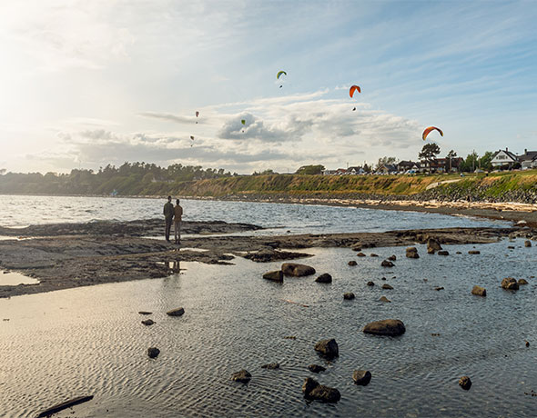 A young couple watches the paragliders at Clover Point in Victoria, BC